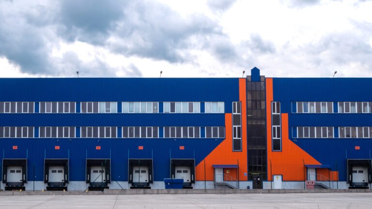 Hubs logísticos - Vista frontal de un almacén logístico con muelles de carga y fachada azul y naranja